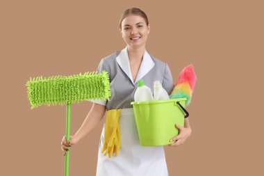 Bej arka planda temizlik malzemeleri olan genç bir hizmetçi.