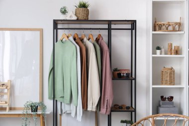 Beyaz duvarın yanında giysi askılığı ve raf ünitesi olan modern soyunma odasının içinde.