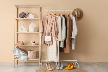 Bej duvarın yanında giysi askılığı ve raf ünitesi olan modern soyunma odasının içinde.