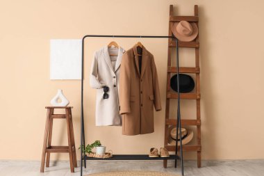 Bej duvarın yanında elbise askısı, merdiven ve sehpası olan modern tuvalet odası.