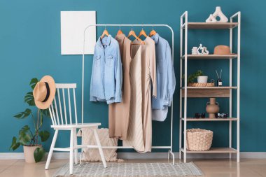 Modern giyinme odasının içinde elbise askılığı, raf ünitesi ve mavi duvarın yanındaki sandalye.