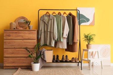 Sarı duvarın yanında elbise askısı ve şifoniyeri olan modern soyunma odasının içinde.