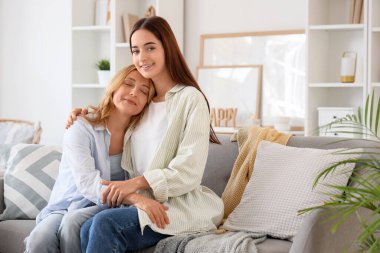 Evdeki kanepede otururken annesine sarılan genç bir kadın. Uluslararası Sarılma Günü