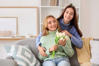 Evde annesine lalelerle sarılan güzel bir genç kadın. Uluslararası Sarılma Günü