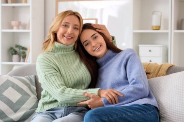 Orta yaşlı bir kadın evdeki kanepede otururken yetişkin kızına sarılıyor. Uluslararası Sarılma Günü