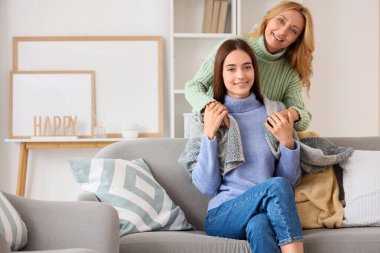 Yetişkin kızını battaniyeyle örten orta yaşlı bir kadın.