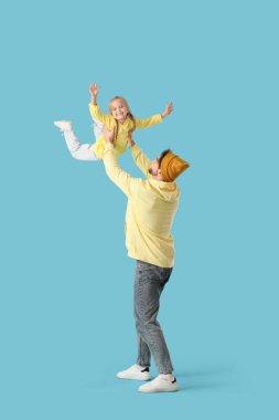 Genç adam mavi arka planda küçük kızıyla oynuyor.