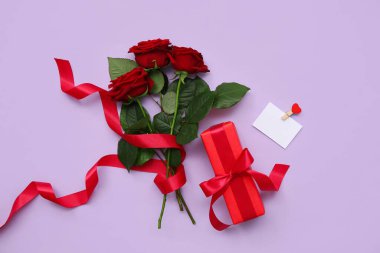 Hediye kutusu ve leylak arkaplanda güzel kırmızı güller olan boş bir kart. Sevgililer Günü kutlaması