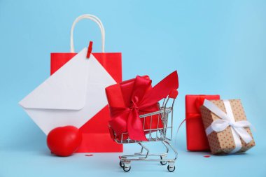 Mini alışveriş arabası, hediye kutuları, kağıt torba ve mavi arka planda zarf. Sevgililer Günü kutlaması