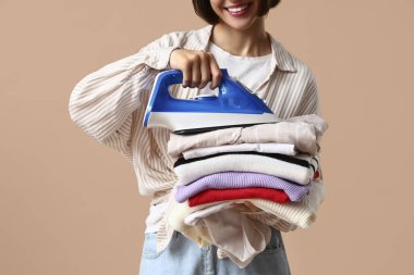 Bej arka planda demir ve giysi yığını ile gülümseyen genç kadın.