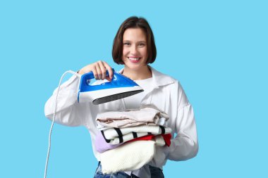 Mavi arka planda bir yığın elbisesi ve demiri olan genç bir kadın.