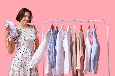 Pembe arka planda, askıların yanında demir tutan genç bir kadın.