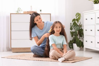 Genç anne banyoda yerde otururken küçük kızının saçlarını tarıyor.