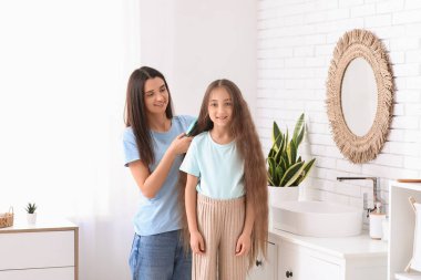 Genç anne banyoda küçük kızının saçını tarıyor.