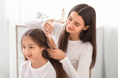 Genç anne banyoda küçük kızının saçını tarıyor.