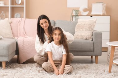 Genç anne evde yerde otururken kızının saçlarını tarıyor.