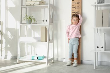 Çocuk doktorunun muayenehanesinde boyunu ölçen sevimli küçük bir kız.