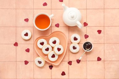 Plate with sweet cookies and cup of tea on beige tile background. Valentine's Day celebration clipart