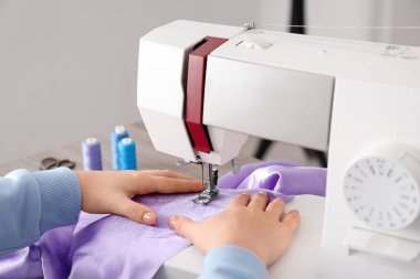 Genç bayan terzi atölyede, yakın plan masadaki leylak kumaş için dikiş makinesi kullanıyor.