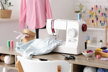 Kot şortlu modern dikiş makinesi ve atölyedeki terzi malzemeleri.