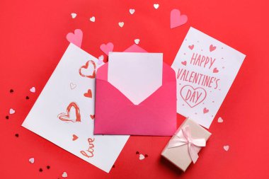 İçinde hediye kartları ve kırmızı arka planda kağıt kalpler olan bir zarf. Sevgililer Günü kutlaması