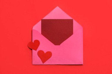 Zarfta boş kart ve kırmızı zemin üzerinde kağıt kalpler var. Sevgililer Günü kutlaması