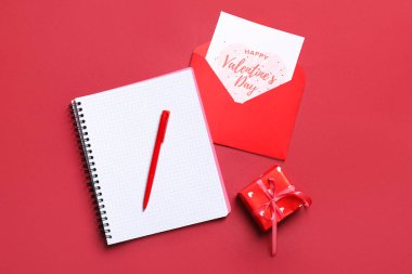 Kırmızı arka planda hediye kartı, kutu ve defter olan zarf. Sevgililer Günü kutlaması