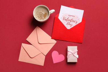 Kırmızı arka planda hediye kartı, kutu ve bir fincan kahve olan zarflar. Sevgililer Günü kutlaması