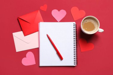 Kırmızı zemin üzerinde defter, kağıt kalpler ve bir fincan kahve olan zarflar. Sevgililer Günü kutlaması