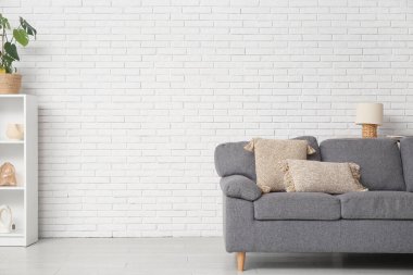 Beyaz tuğla duvarın yanında rahat kanepesi ve raf ünitesi olan şık bir oturma odası.