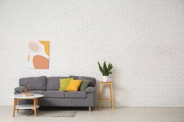 Rahat kanepesi, sehpası ve beyaz tuğla duvarın yanında bitkisi olan şık bir oturma odası.