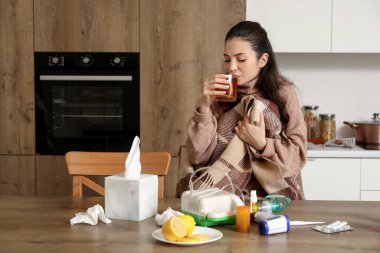 Ekoseli genç bir kadın mutfakta limon çayı içiyor.