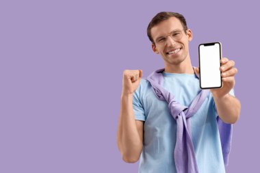 Leylak arka planında boş cep telefonu olan mutlu genç bir adam.