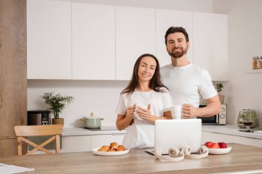 Mutfaktaki masada kahve ve dizüstü bilgisayarı olan sevimli bir çift.