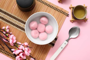 Bambu hasırı, bir kase tangyuan, pembe arka planda çay ve sakura, yakın plan. Dongzhi Festivali