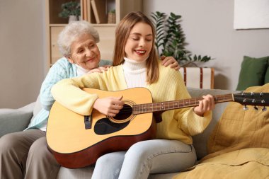 Evde gitar çalarak torununa sarılan son sınıf öğrencisi kadın.