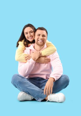 Mutlu genç çift mavi arka planda sarılıyor