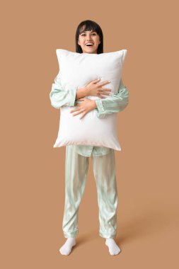 Kahverengi arka planda yumuşak yastıklı pijamalı güzel bir kadın.