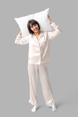 Gri arka planda yumuşak yastıklı pijamalı mutlu genç kadın.