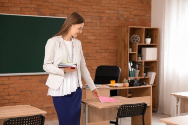 Bayan öğretmen sınıfın masasına kitap koyuyor.