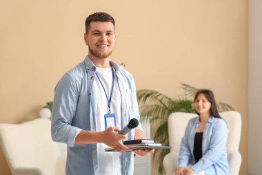 Mikrofonlu ve defterli bir erkek muhabir stüdyoda genç bir kadınla röportaj yapıyor.