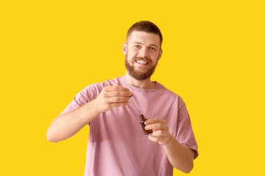 Sarı arka planda saç büyümesi için serumu olan mutlu genç adam.