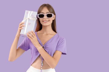 Mor arka planda hediye kutusu olan güzel bir genç kadın.