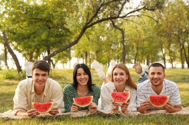 Parkta piknik yaparken ellerinde karpuz dilimleri olan genç arkadaşlar