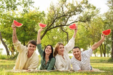 Parkta piknik yaparken ellerinde karpuz dilimleri olan genç arkadaşlar