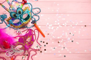 Pembe ahşap arka planda parti boynuzları, konfeti ve boncukları olan güzel karnaval maskeleri. Üst görünüm