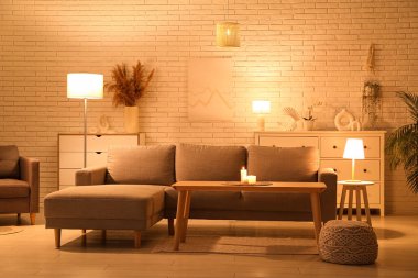 Geceleri rahat kanepesi, puf ve parlayan lambaları olan modern bir oturma odası.