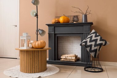 Sonbahar salonunda siyah şömine, sehpa, yastık ve balkabağı.