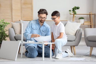 Babası talimatlarla ve küçük oğlu da evde raf montajı yapıyor.