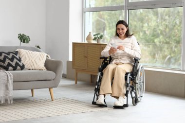 Tekerlekli sandalyedeki genç kadın evde cep telefonu kullanıyor.